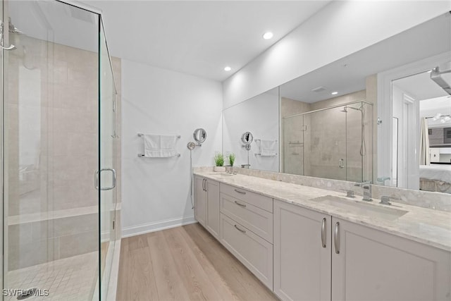 bathroom featuring a stall shower, double vanity, a sink, and wood finished floors