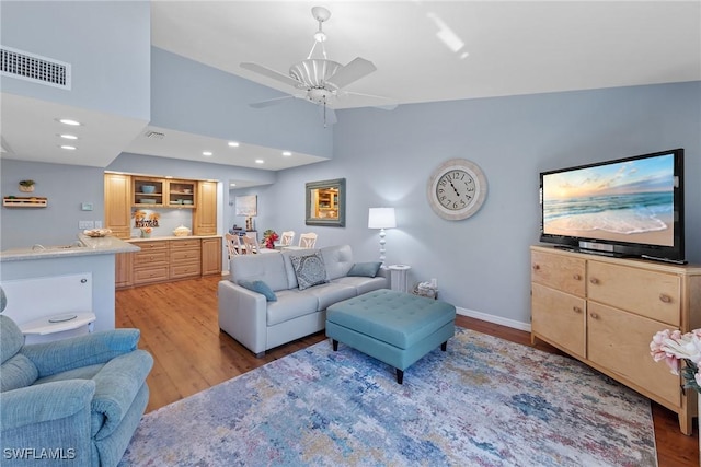 living room featuring a ceiling fan, light wood-type flooring, visible vents, and baseboards