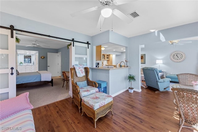 living room featuring a barn door, visible vents, a ceiling fan, and wood finished floors