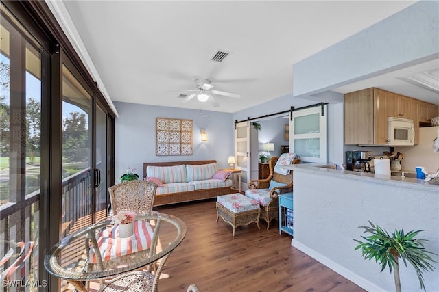 living area featuring a ceiling fan, a barn door, visible vents, and wood finished floors