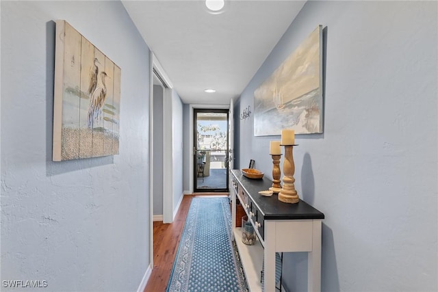 hallway with a textured wall, baseboards, and wood finished floors