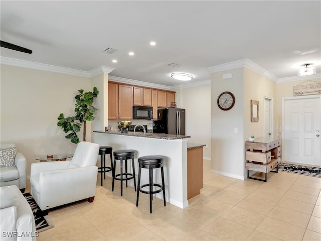 kitchen featuring black microwave, a breakfast bar area, freestanding refrigerator, dark stone countertops, and crown molding