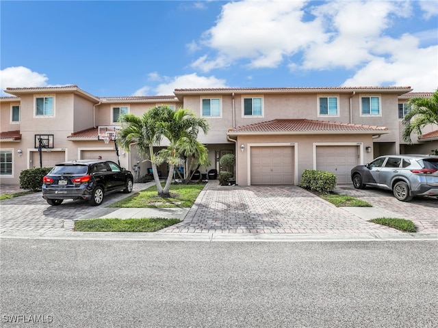 townhome / multi-family property featuring a garage, a tiled roof, decorative driveway, and stucco siding