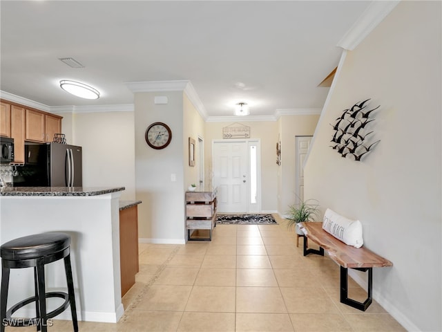 kitchen featuring ornamental molding, freestanding refrigerator, light tile patterned flooring, dark stone countertops, and black microwave