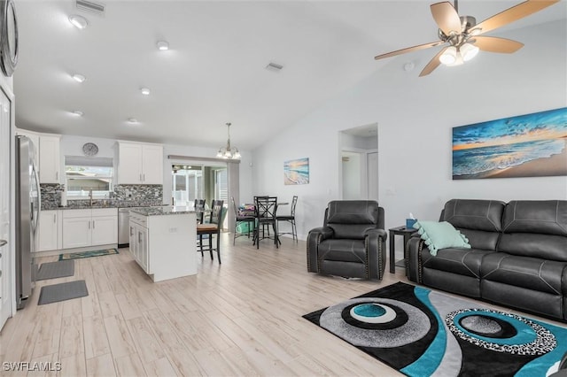 living area featuring lofted ceiling, light wood-style flooring, ceiling fan with notable chandelier, and visible vents