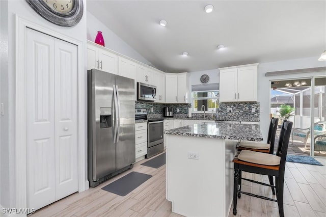 kitchen with stainless steel appliances, a kitchen island, a sink, white cabinets, and dark stone countertops