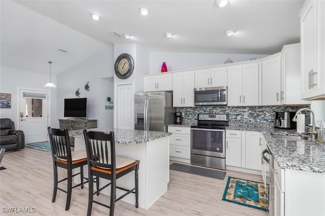 kitchen featuring stainless steel appliances, a kitchen island, a sink, white cabinetry, and open floor plan