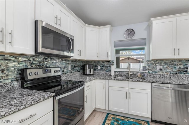 kitchen featuring stainless steel appliances, stone counters, white cabinets, and a sink