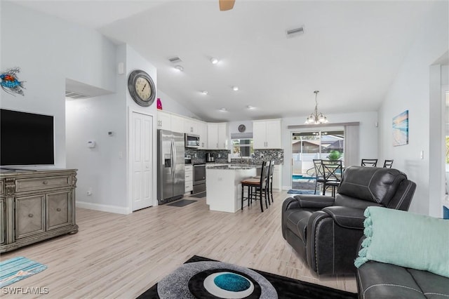 living room featuring baseboards, visible vents, light wood-type flooring, high vaulted ceiling, and a notable chandelier