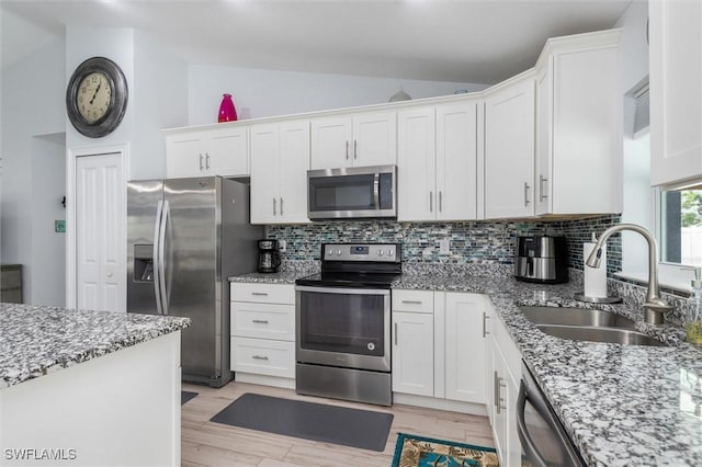 kitchen with lofted ceiling, stainless steel appliances, a sink, white cabinetry, and backsplash