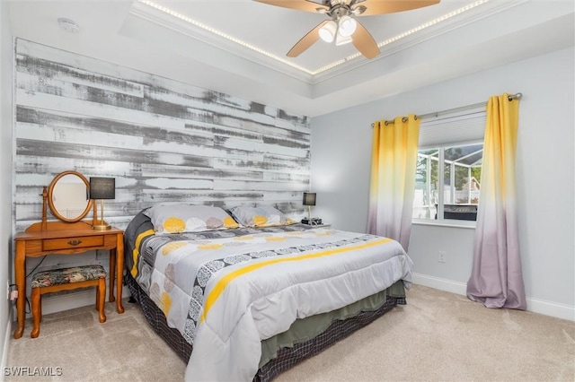 bedroom featuring a tray ceiling, an accent wall, light carpet, ceiling fan, and baseboards