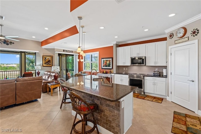 kitchen featuring backsplash, appliances with stainless steel finishes, open floor plan, white cabinetry, and a kitchen bar