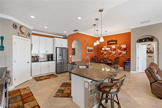 kitchen featuring arched walkways, decorative backsplash, appliances with stainless steel finishes, a breakfast bar area, and a sink