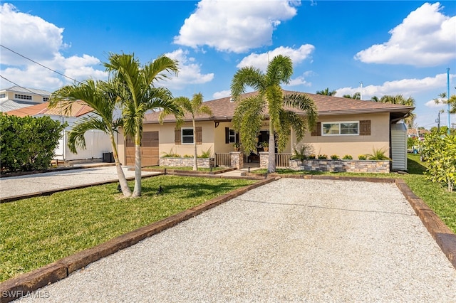 ranch-style house featuring gravel driveway, an attached garage, a front lawn, and stucco siding