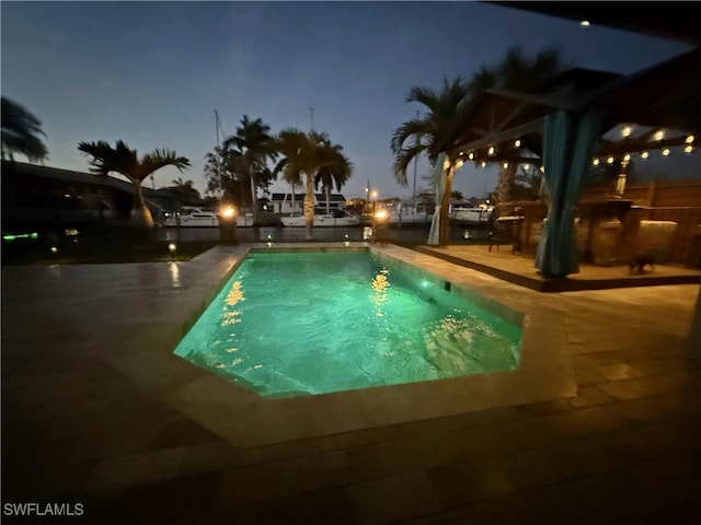 pool at night with a patio and a fenced in pool