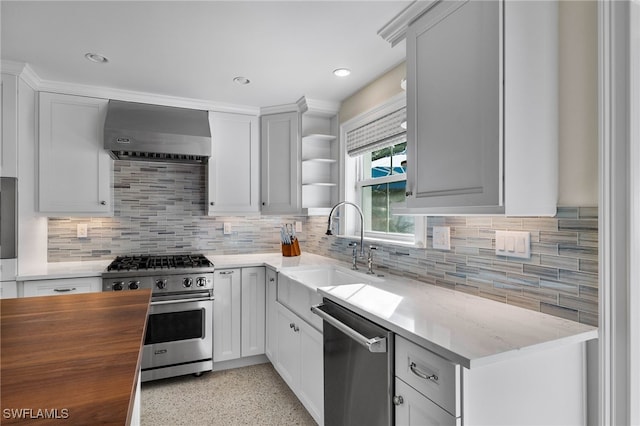 kitchen featuring tasteful backsplash, appliances with stainless steel finishes, wall chimney range hood, open shelves, and a sink