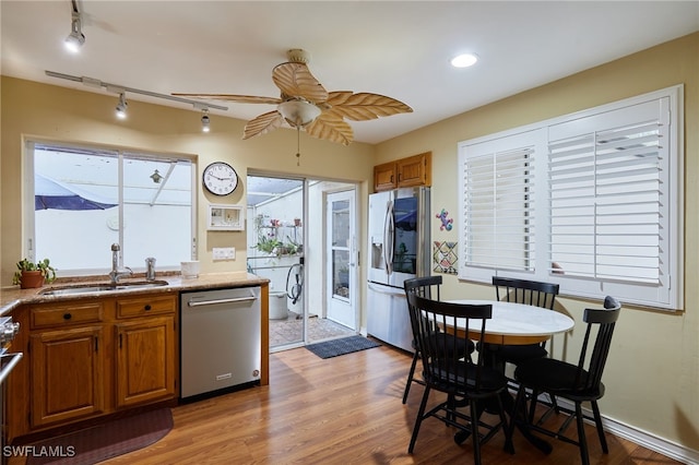 kitchen featuring stainless steel appliances, a sink, a ceiling fan, light wood finished floors, and brown cabinetry