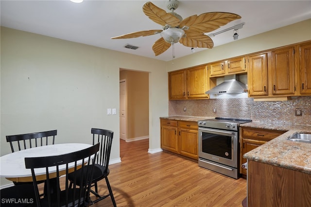 kitchen featuring light wood-type flooring, wall chimney range hood, stainless steel electric range oven, and tasteful backsplash