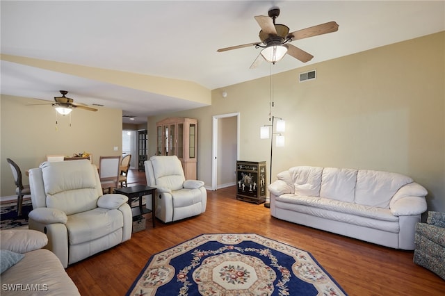 living room featuring lofted ceiling, wood finished floors, visible vents, baseboards, and a ceiling fan