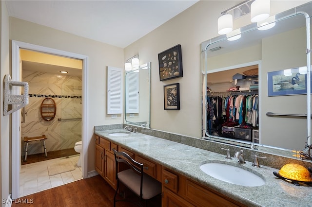 full bathroom featuring double vanity, a tile shower, a sink, and wood finished floors