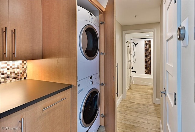 laundry area featuring stacked washer and dryer, baseboards, and light wood finished floors