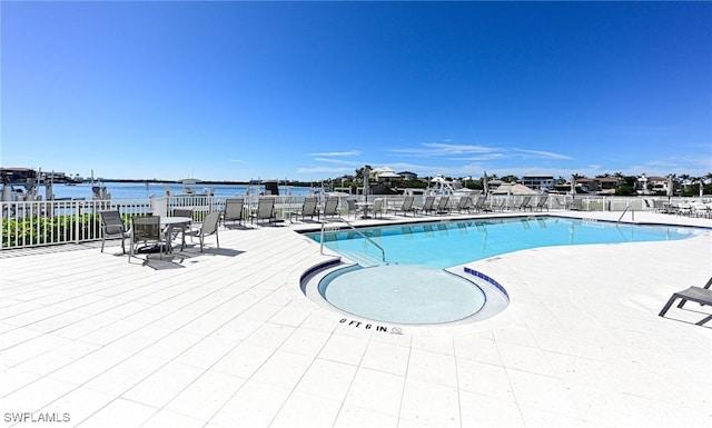 community pool with a patio area, a water view, and fence