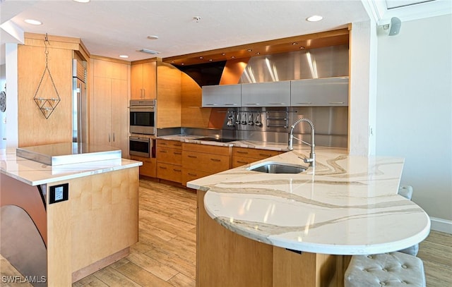 kitchen with light wood-style flooring, a peninsula, a sink, and appliances with stainless steel finishes