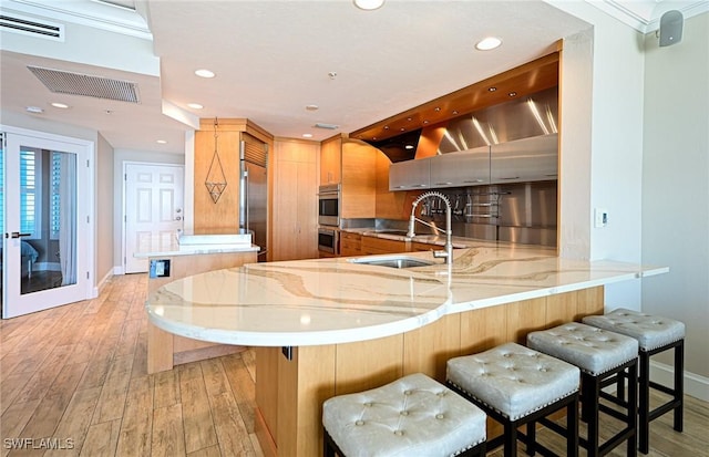 kitchen with visible vents, a peninsula, light stone countertops, appliances with stainless steel finishes, and light wood-type flooring