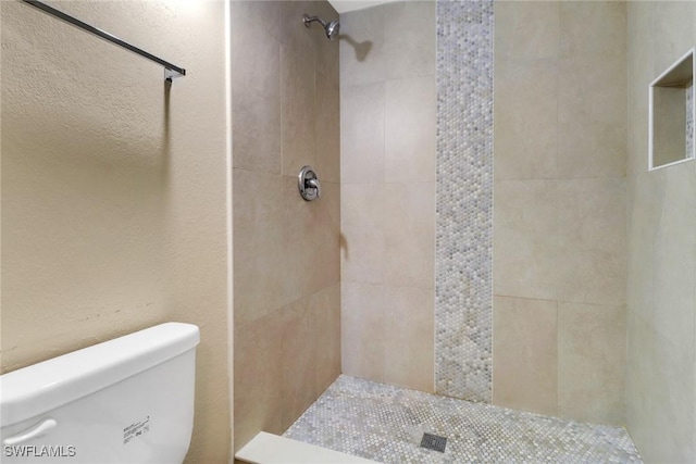 bathroom with tiled shower, a textured wall, and toilet