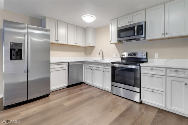 kitchen featuring appliances with stainless steel finishes, light wood-type flooring, a sink, and white cabinetry