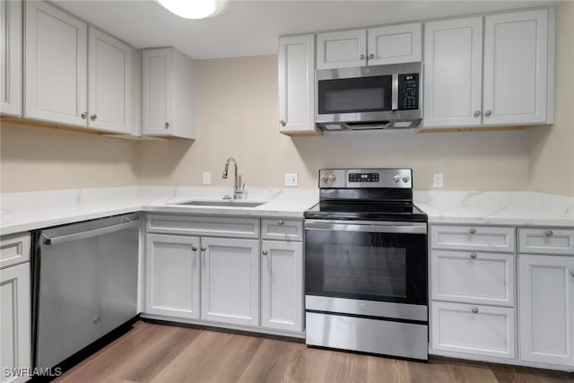 kitchen with appliances with stainless steel finishes, white cabinetry, a sink, and light wood-style flooring