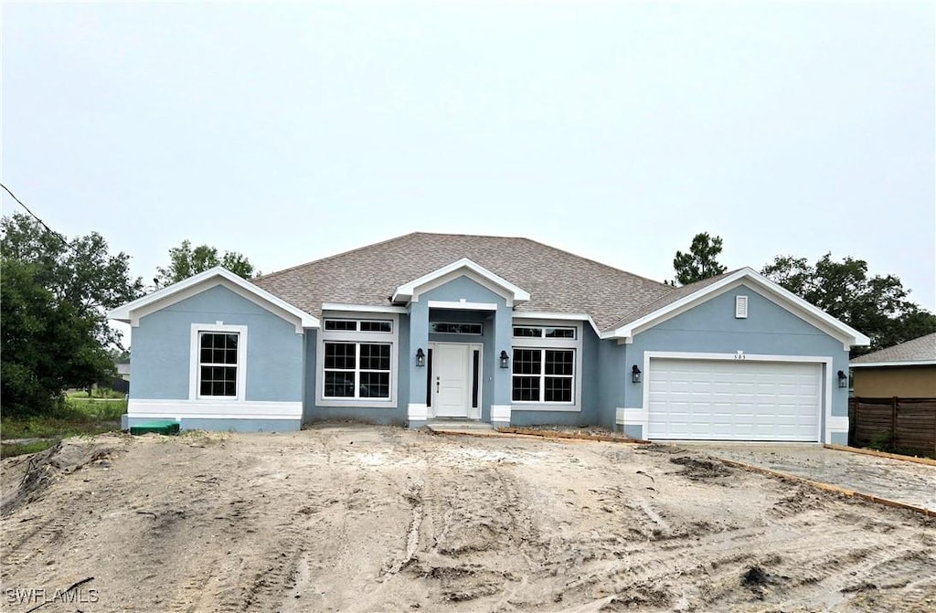 565 Windermere Dr, Lehigh Acres, FL 33972 - view of front facade with stucco siding, a garage, a shingled roof, and concrete driveway