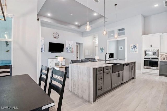 kitchen featuring gray cabinetry, a sink, open floor plan, appliances with stainless steel finishes, and a center island with sink