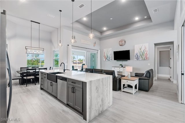 kitchen featuring light stone counters, gray cabinetry, stainless steel appliances, a center island with sink, and pendant lighting