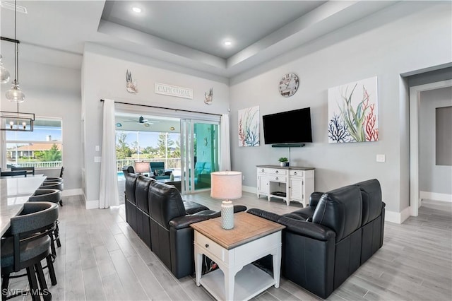 living room with light wood-type flooring, a tray ceiling, and baseboards