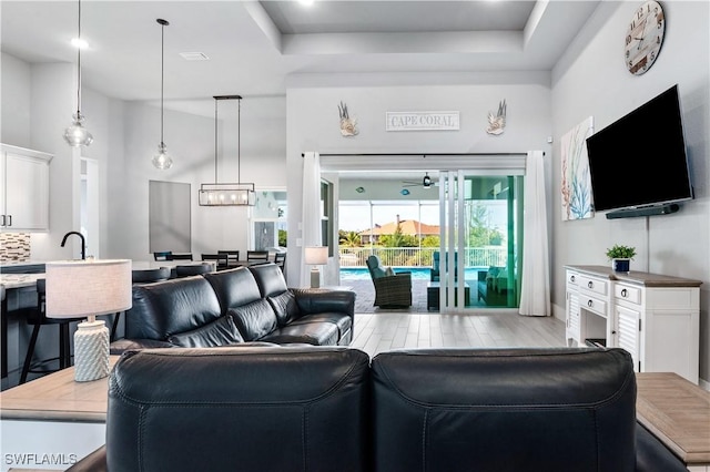 living room with light wood-style floors, a high ceiling, and a tray ceiling