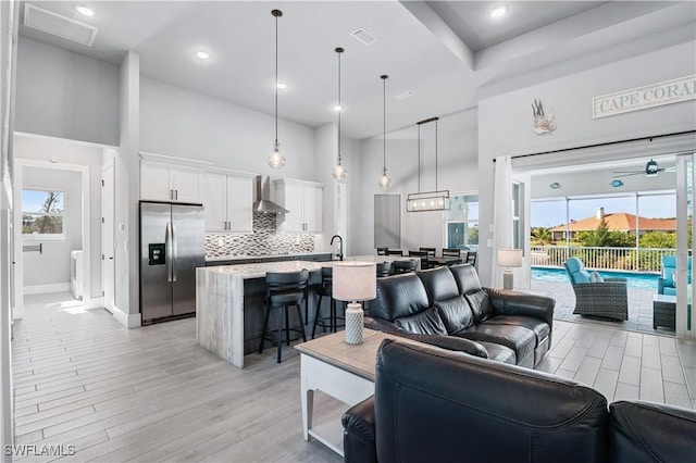 living room with light wood finished floors, baseboards, visible vents, ceiling fan, and a high ceiling