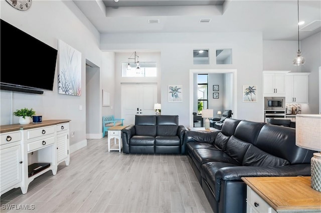 living room featuring light wood-type flooring, a towering ceiling, visible vents, and a wealth of natural light