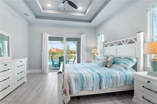 bedroom featuring access to exterior, visible vents, a tray ceiling, and wood finish floors