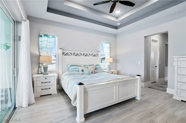 bedroom featuring wood tiled floor, a tray ceiling, ceiling fan, and baseboards