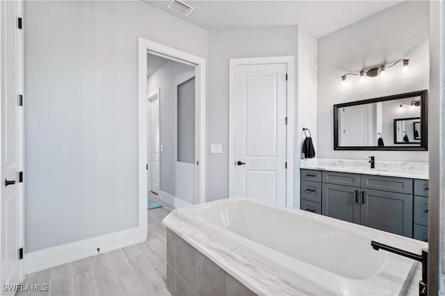 full bathroom featuring tiled bath, baseboards, visible vents, wood finished floors, and vanity