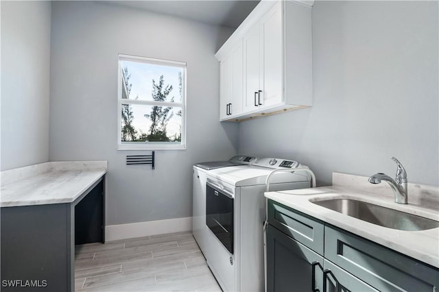 washroom featuring washing machine and dryer, wood finish floors, a sink, baseboards, and cabinet space