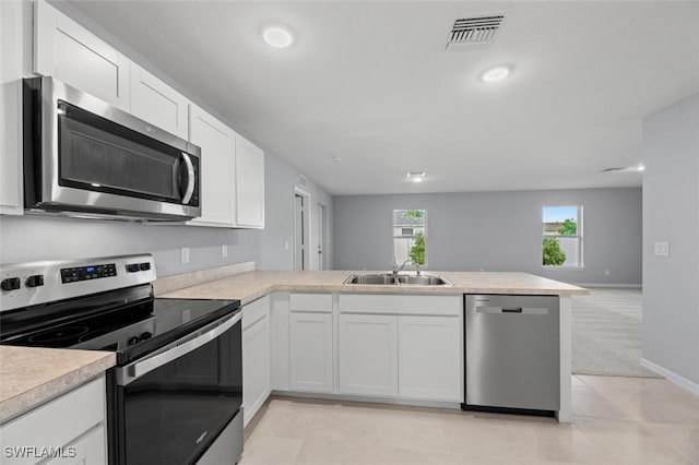 kitchen with light countertops, appliances with stainless steel finishes, white cabinets, a sink, and a peninsula