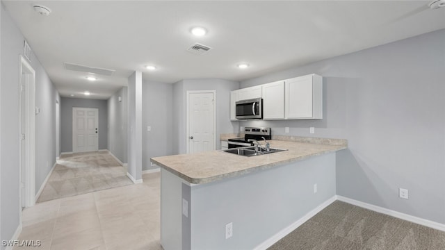 kitchen featuring stainless steel appliances, a peninsula, a sink, white cabinetry, and light countertops