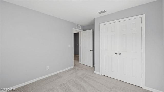 unfurnished bedroom with a closet, light colored carpet, visible vents, and baseboards