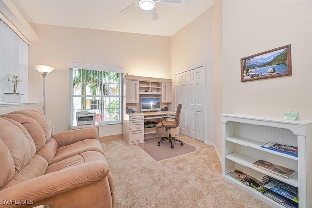 home office featuring a towering ceiling, ceiling fan, baseboards, and light colored carpet