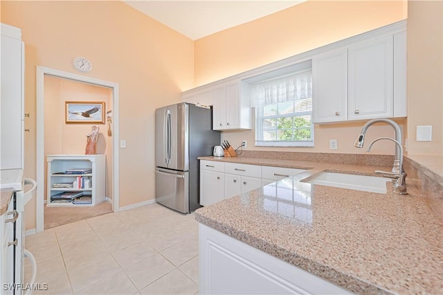 kitchen featuring light stone counters, freestanding refrigerator, white cabinets, and a sink