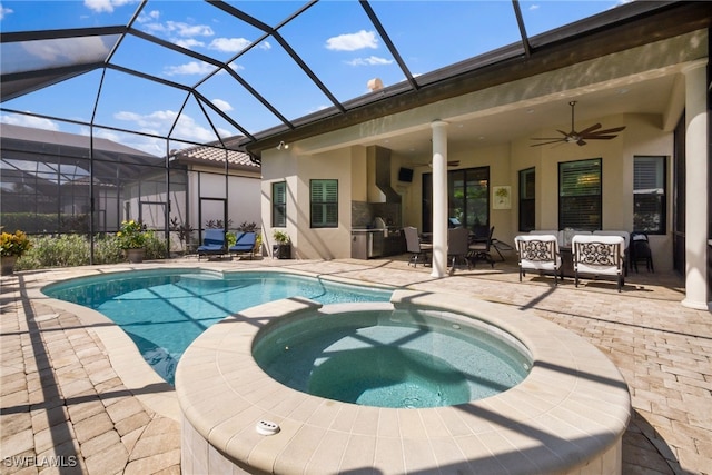 view of swimming pool featuring a patio, a pool with connected hot tub, an outdoor kitchen, glass enclosure, and ceiling fan