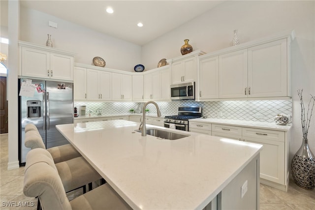 kitchen with white cabinets, appliances with stainless steel finishes, a breakfast bar, a kitchen island with sink, and a sink