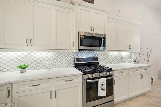 kitchen featuring tasteful backsplash, appliances with stainless steel finishes, white cabinetry, light tile patterned flooring, and light stone countertops